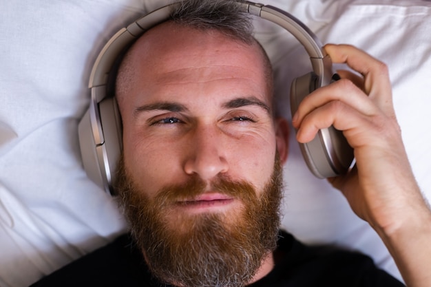 Hombre caucásico feliz en la cama con auriculares escuchando disfrutar de su música favorita, descansando solo, bailando.