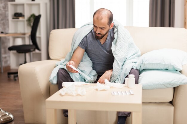 Hombre caucásico con fiebre cubierto con una manta durante la pandemia mundial.