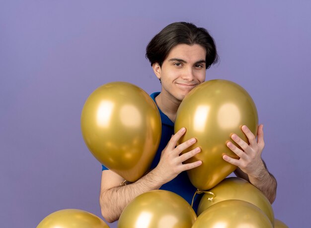 Hombre caucásico guapo complacido está parado con globos de helio