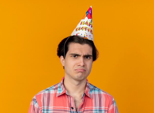 Hombre caucásico guapo disgustado con gorro de cumpleaños mira a la cámara