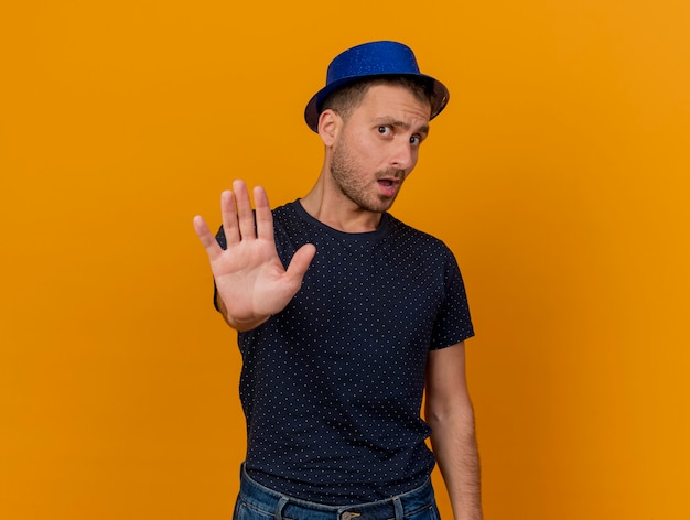 Foto gratuita hombre caucásico guapo disgustado vestido con gorro de fiesta azul gestos dejar señal de mano aislada sobre fondo naranja con espacio de copia