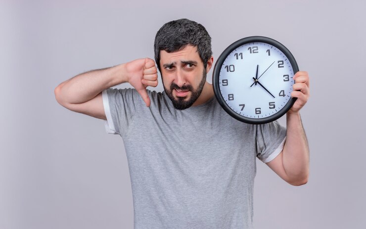 Foto gratuito hombre caucásico guapo joven disgustado sosteniendo el reloj apuntando hacia abajo y mirando al lado aislado sobre fondo blanco.