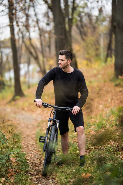 Hombre caucásico joven atractivo que monta en bicicleta en el parque. Al aire libre, otoño otoño parque. Copia espacio