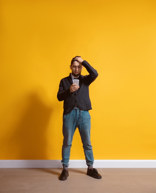 Hombre caucásico joven con retrato de cuerpo entero de smartphone aislado sobre pared amarilla