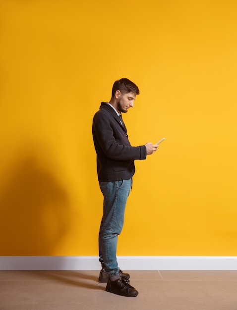 Hombre caucásico joven con retrato de cuerpo entero de smartphone sobre amarillo