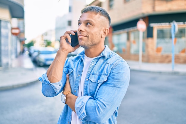 Hombre caucásico joven sonriendo feliz hablando en el teléfono inteligente en la ciudad