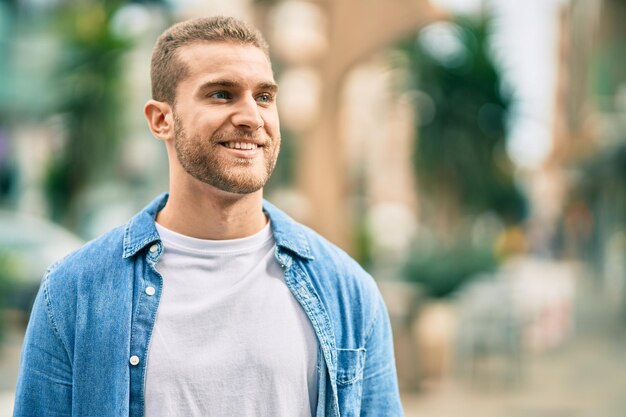 Hombre caucásico joven sonriendo feliz de pie en la ciudad.