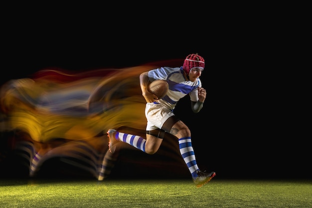 Un hombre caucásico jugando al rugby en el estadio con luz mixta. Colocar al joven jugador en movimiento o acción durante el juego deportivo. Concepto de movimiento, deporte, estilo de vida saludable.