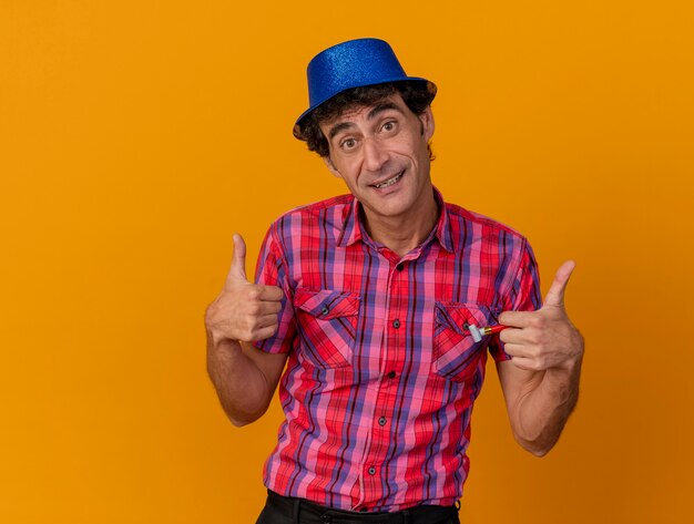 Hombre caucásico de mediana edad complacido con gorro de fiesta mirando a la cámara mostrando los pulgares para arriba aislado sobre fondo naranja con espacio de copia