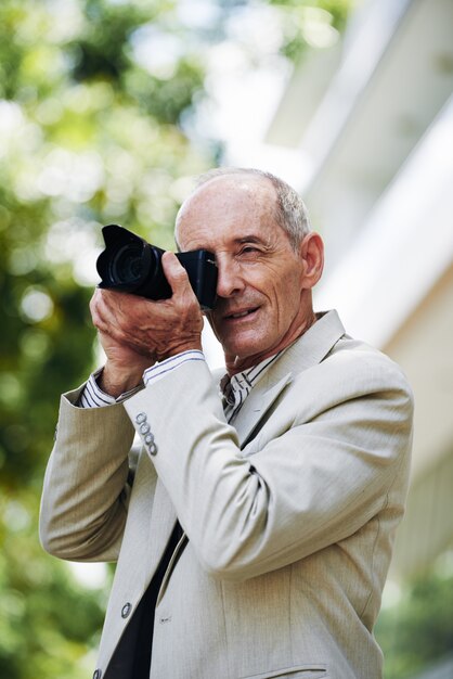 Hombre caucásico de mediana edad tomando fotos en la calle con cámara digital profesional