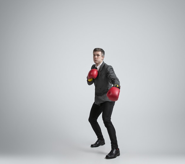Hombre caucásico en ropa de oficina de boxeo con dos guantes rojos sobre fondo gris.