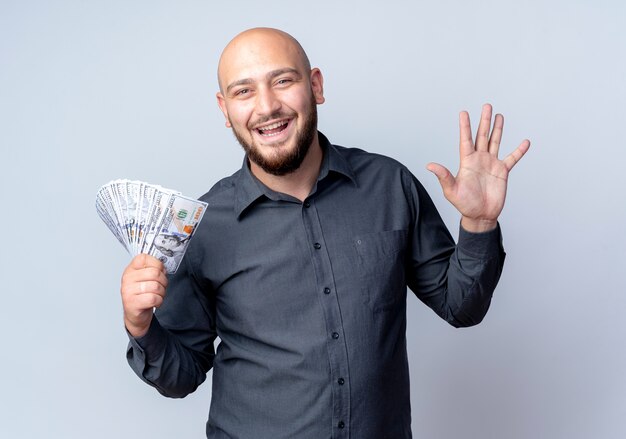 Hombre de centro de llamadas calvo joven alegre que sostiene el dinero y que muestra cinco con la mano aislada en blanco