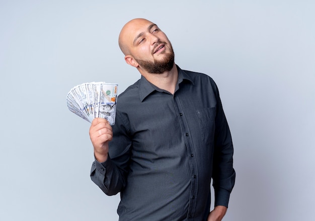 Hombre de centro de llamadas calvo joven confiado con dinero mirando hacia arriba aislado en blanco con espacio de copia