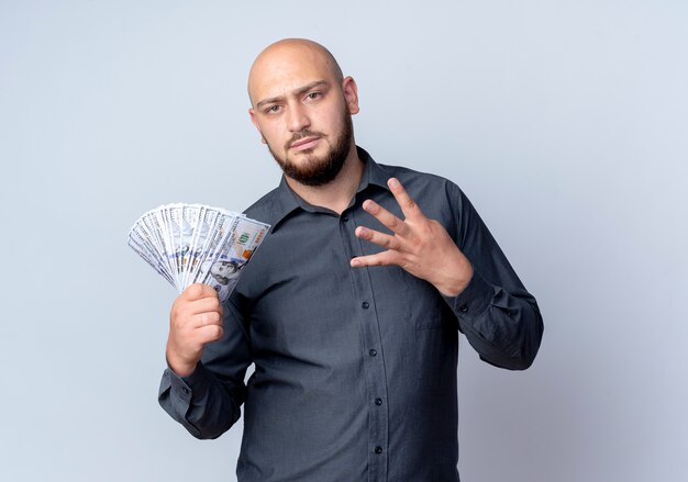 Hombre de centro de llamadas calvo joven disgustado sosteniendo dinero y mostrando cuatro aislado sobre fondo blanco.