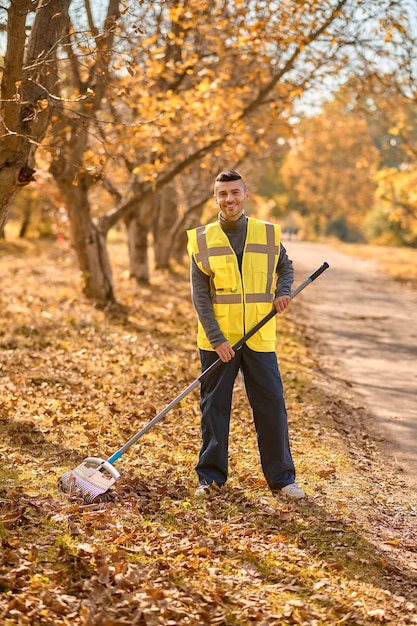 Un hombre con un chaleco amarillo rastrillar las hojas en el parque
