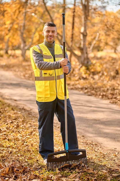 Un hombre con un chaleco amarillo con rastrillo en el parque.