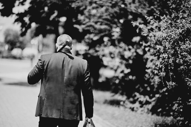 Hombre en chaqueta con cabeza de calavera de bastón sobre hombros y bolso en mano Blanco y negro