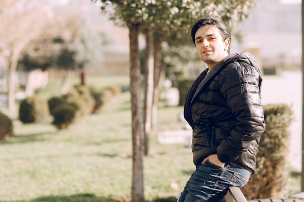 Hombre con chaqueta de cuero poniendo las manos en el bolsillo y de pie en el parque. Foto de alta calidad