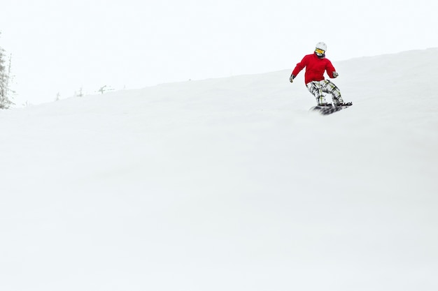 Hombre en chaqueta de esquí roja baja la colina en su tabla de snowboard