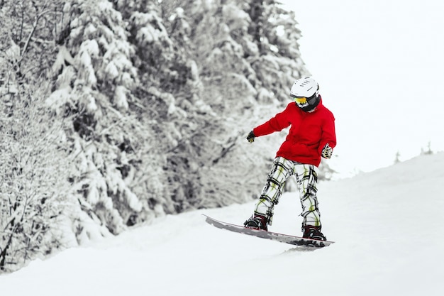 Hombre en chaqueta de esquí roja baja la colina en su tabla de snowboard