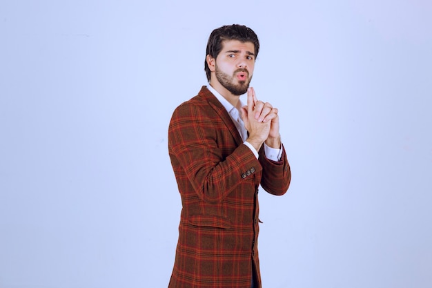 Hombre de chaqueta marrón haciendo signo de pistola.