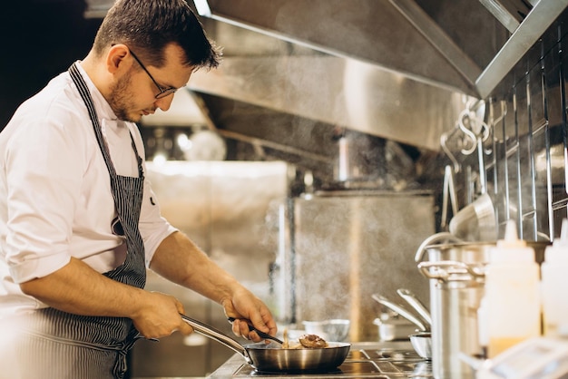 Hombre chef freír carne en una sartén al fuego