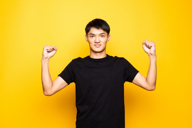 Hombre chino asiático joven que celebra sorprendido y asombrado por el éxito con los brazos levantados y los ojos abiertos que se colocan sobre la pared amarilla aislada. Concepto ganador.