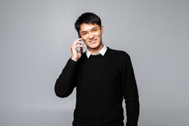 Hombre chino feliz que usa un smartphone aislado contra la pared blanca.