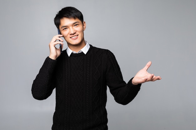 Hombre chino feliz que usa un smartphone aislado contra la pared blanca.