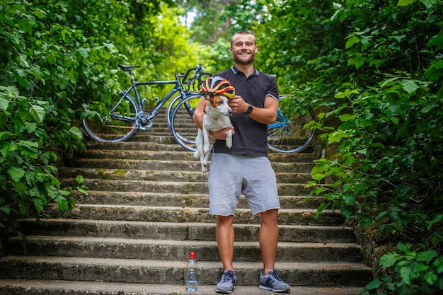 Hombre ciclista posando con su perro russel en las escaleras de un bosque.