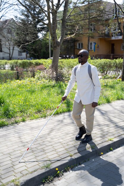 Hombre ciego de tiro completo caminando con bastón blanco