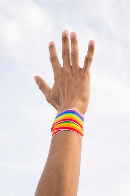 Hombre con cinta en colores LGBT en mano y cielo azul.