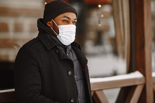 Hombre en una ciudad de invierno. Chico con un abrigo negro. Hombre con una máscara médica.