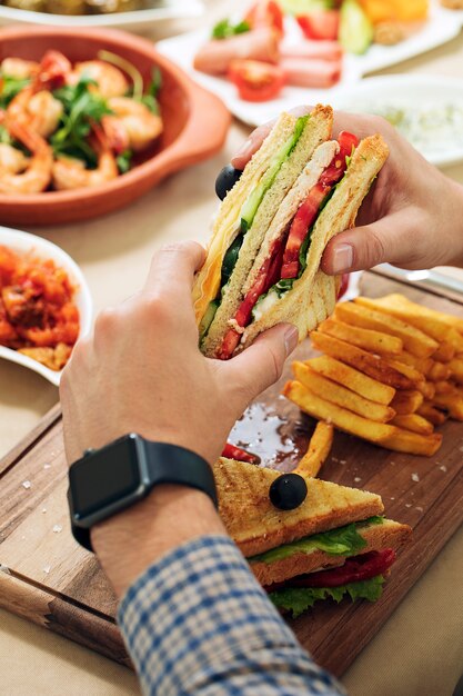 Hombre con club sandwich en las manos junto a una mesa.