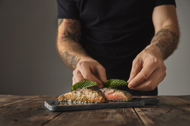 El hombre cocina comida saludable en la mesa rústica, decorar con hojas de menta dos piezas crudas de salmón en salsa de vino blanco con especias y hierbas presentadas en una cubierta de mármol preparada para parrilla