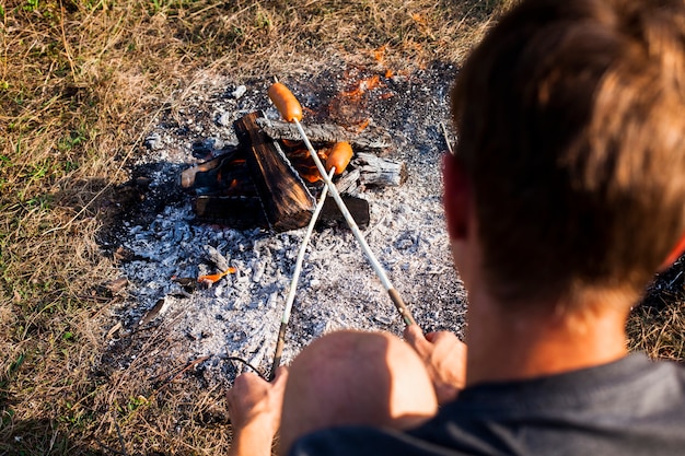 Hombre cocinando salchichas sobre el hombro