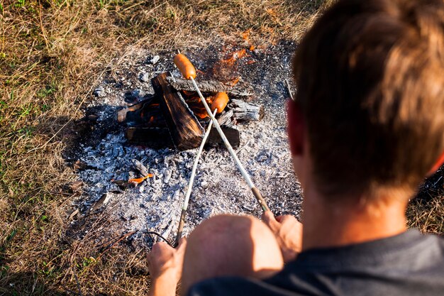 Hombre cocinando salchichas sobre el hombro