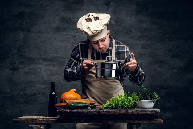 Un hombre cocinando una sopa y probándola en un fondo oscuro.