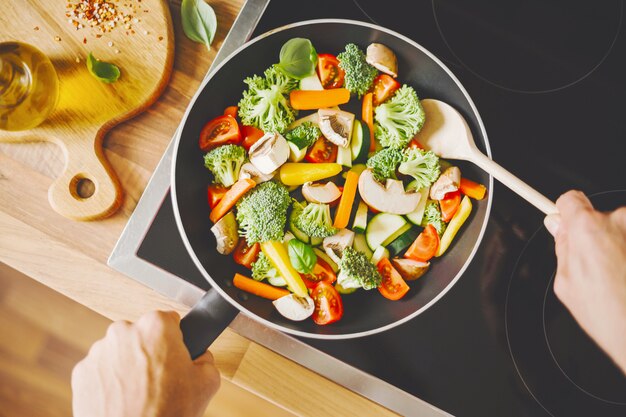 Hombre cocinando verduras frescas en la sartén