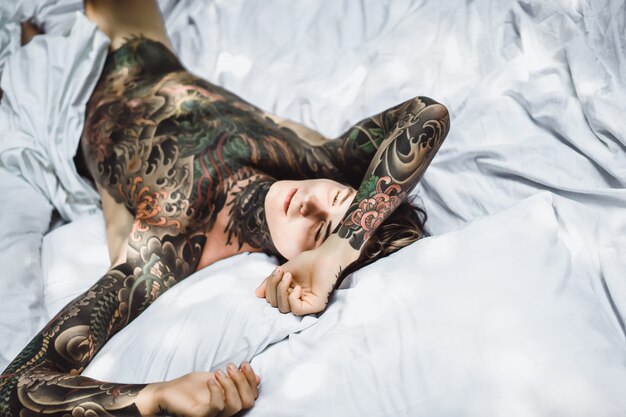 Hombre con coloridos tatuajes descansando sobre una sábana blanca