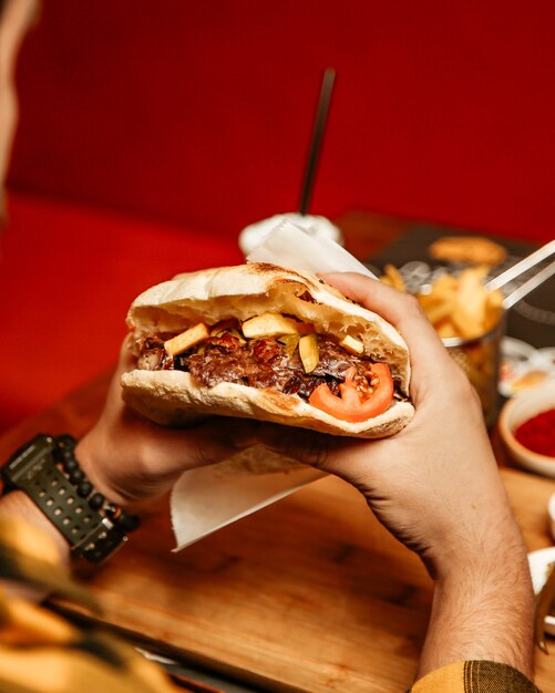 El hombre come doner en pan con carne, tomate y papas fritas