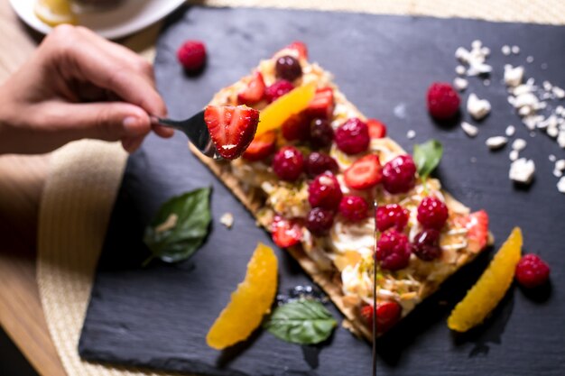 El hombre come tarta de napoleón con crema de frambuesa, naranja, cereza, malvaviscos, vista lateral de menta