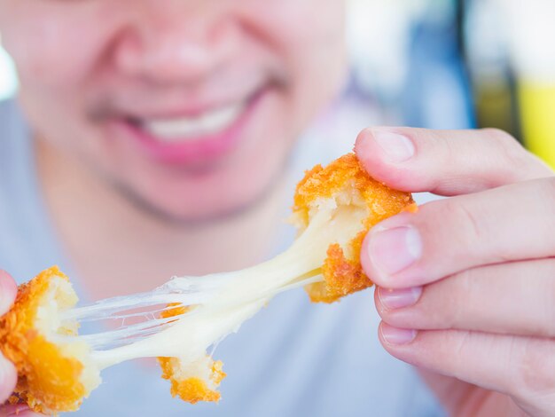 El hombre va a comer pegajosa bola de queso frito estirado.