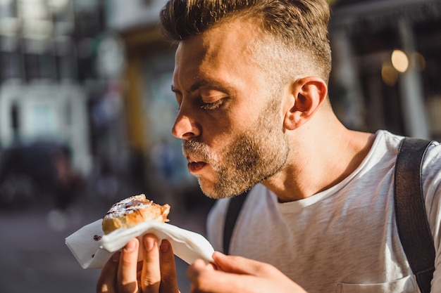 Hombre comiendo gofres holandeses en la calle cerca de café. Comida callejera en Holanda.