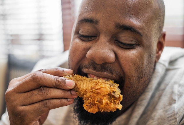 Hombre comiendo un pedazo de pollo frito