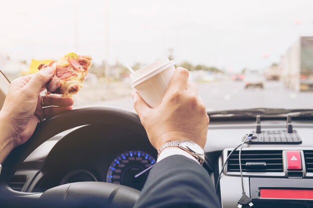 Hombre comiendo pizza y café mientras conduce un auto peligrosamente