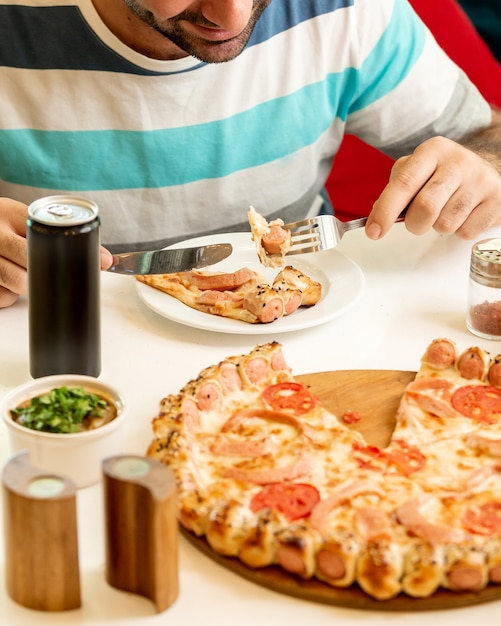 Foto gratuita hombre comiendo una rebanada de pizza de salchicha en el restaurante