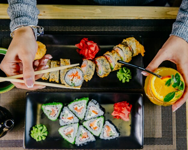 Hombre comiendo sushi unagi maki con vista superior de cóctel de naranja