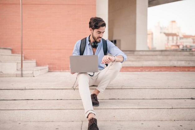 Hombre con la computadora portátil mirando la hora de reloj