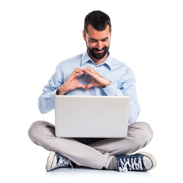 Hombre con la computadora portátil que hace un corazón con sus manos